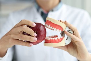 Dentist holding a dental crown model and a red apple while explaining foods to avoid after getting a new dental crown