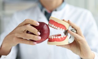 Dentist holding a dental crown model and a red apple while explaining foods to avoid after getting a new dental crown
