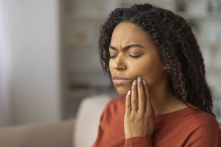 Young woman holding her jaw in pain due to an intermittent toothache at home